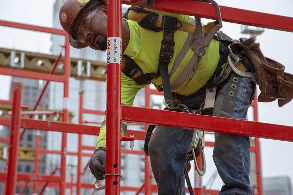 Man installing clips on red scaffolding.