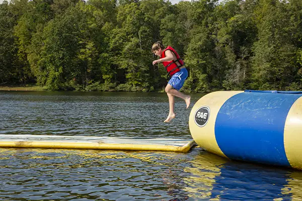 Boy, at camp is playing on floatation devices at the lake.