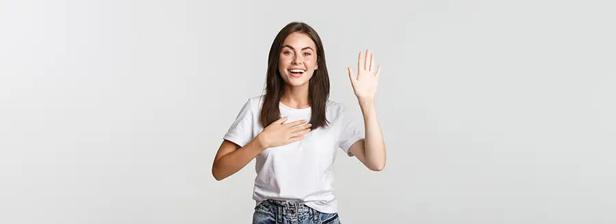 Cute young lady smiling and holding up her left hand with her right hand on her chest.