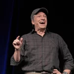 Mike Rowe laughing on stage and using his fingers to indicate how small something is