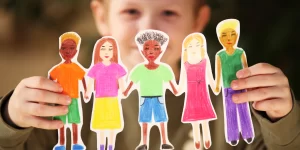 Child holding up color, paper cutouts of a diverse group of kids.